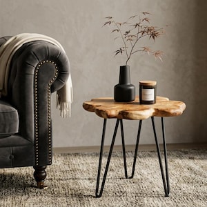 May include: A dark gray tufted sofa with a cream-colored throw blanket. A live-edge wooden side table with black hairpin legs holds a black vase with branches and a small candle. The scene is set on a textured rug.