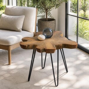 May include: A side table featuring a natural, irregular-shaped wooden slab top with a smooth, light brown finish. The table is supported by three slender, black metal hairpin legs. A small, round, white stone object and a dark glass bowl sit on top.