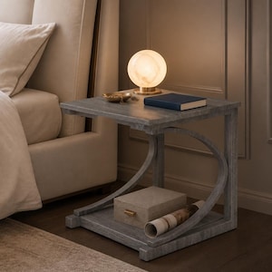 May include: A gray wooden side table with a curved support frame, featuring a spherical lamp, a small gold bowl, and a dark blue book on the top surface, with a rectangular beige box and a rolled paper document on the lower shelf.
