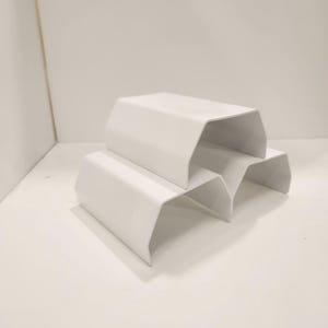 Könnte beinhalten: Drei weiße, geometrische, bogenförmige Präsentationsständer sind auf einer weißen Oberfläche gestapelt. Die Ständer haben ein klares, modernes Design mit einer glatten, matten Oberfläche. Die Ständer sind versetzt angeordnet und erzeugen eine ansprechende Präsentation.