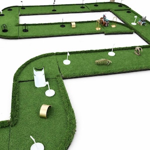 Puede incluir: Juego de minigolf en miniatura con c&eacute;sped verde, banderas negras y varios obst&aacute;culos. Incluye aros dorados, marcadores de tee blancos y elementos decorativos como un esqueleto de dinosaurio y figuritas.