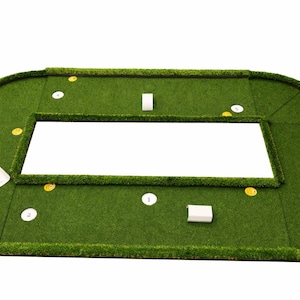 Puede incluir: Una alfombra de putting verde con un recorte rectangular en el centro. La alfombra tiene un borde curvo e incluye marcadores blancos y amarillos, y dos bloques blancos. Dise&ntilde;ado para la pr&aacute;ctica de golf.