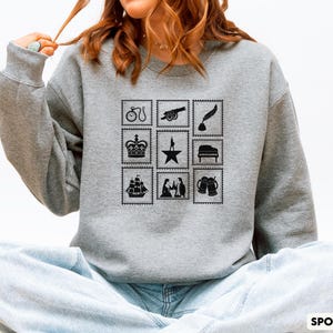 Puede incluir: Sudadera gris deportiva con un dise&ntilde;o de sellos negros. Los sellos representan una bicicleta, un ca&ntilde;&oacute;n, una pluma, una corona, una estrella, un piano, un barco, figuras y jarras de cerveza. El texto "SPORT GREY" est&aacute; en la parte inferior derecha.
