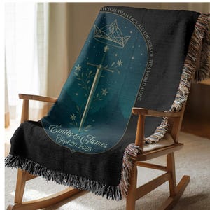 Op de afbeelding: Een zwarte sprei met een teal en marineblauw ontwerp, gedrapeerd over een houten schommelstoel. De sprei heeft een zwaard, een kroon en bloemmotieven. Tekst bevat "Emily & James Sept 20, 2025" en "I'd rather face all the ages of this world alone."