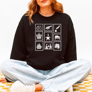 Puede incluir: Sudadera negra con nueve ilustraciones de sellos postales blancos. Los sellos representan una bicicleta, un ca&ntilde;&oacute;n, una pluma, una corona, una estrella, un piano, un barco, figuras y jarras de cerveza. La palabra "BLACK" est&aacute; impresa en la parte inferior derecha.
