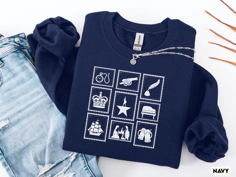 Puede incluir: Sudadera azul marino con un dise&ntilde;o de sellos postales blancos. Los sellos representan un reloj, un ca&ntilde;&oacute;n, una pluma, una corona, una estrella, un piano, un barco, figuras y jarras de cerveza. Un collar plateado con un colgante est&aacute; sobre la sudadera.