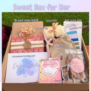 May include: A gift box labeled "Sweet Box for Her" filled with a brand new book, cozy socks, a hair claw clip, a book review sheet, a personalized greeting card, chocolate, tea, sea salted caramel, and magnetic bookmarks. The card says "Enjoy Reading".