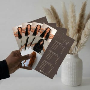 A warm neutral lifestyle shot showing hands holding the printed dark brown luxury price list alongside dried pampas grass and a soft beige background representing the premium printed finish of the luxury hair salon service menu template giving wig seller, extension brand, and beauty professional a visual of how polished their printed price list will look