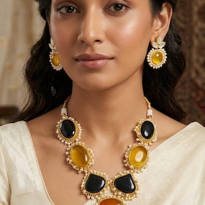 Puede incluir: Un conjunto de collar y pendientes en tono dorado con piedras ovaladas y en forma de lágrima de colores negro, amarillo y ámbar. Las piezas de joyería están adornadas con pequeñas perlas blancas y engastes de metal dorado alrededor.