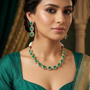 Può includere: Una donna indossa un set di gioielli verde smeraldo abbinato. Il set comprende una collana e orecchini, ciascuno con pietre verdi a forma di goccia incastonate in oro. La donna indossa un top verde.