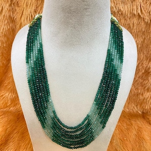 Puede incluir: Un collar de múltiples hilos exhibido en un maniquí. El collar presenta pequeñas cuentas facetadas en diferentes tonos de verde, creando un efecto degradado. Las cuentas están ensartadas, formando múltiples capas que caen en cascada. El collar es una joya.