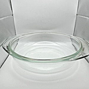 May include: A clear, round glass baking dish with two handles. The dish is made of transparent glass, allowing visibility of the contents. The design is simple and functional, suitable for baking and serving.