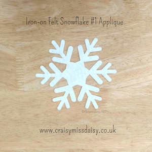 May include: A white iron-on felt snowflake applique. The snowflake has six symmetrical arms with detailed cutouts. The text "Iron-on Felt Snowflake #1 Applique" is at the top. The website address www.craisymissdaisy.co.uk is at the bottom.