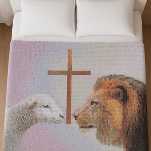 Puede incluir: Una manta suave y texturizada con una cruz, un cordero y un león. La manta tiene una combinación de colores pastel con un fondo lila claro y azul. El cordero y el león se enfrentan, con la cruz en medio.