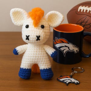 May include: A handmade, white crochet horse with orange hair and blue hooves. A navy blue mug with an orange and white logo, a football, and a keychain with the same logo are also present.