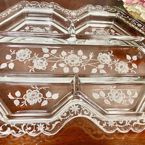 May include: Clear glass serving tray with four compartments and a decorative floral design. The tray has a scalloped edge and etched floral patterns. The tray is designed for serving appetizers or snacks.