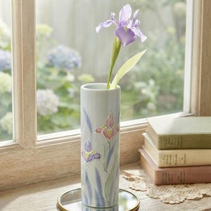 May include: A cylindrical light blue ceramic vase featuring raised, hand-painted iris flower motifs in shades of pink, purple, and green. The vase holds a single purple iris flower and sits on a small, round, gold-rimmed mirror base.