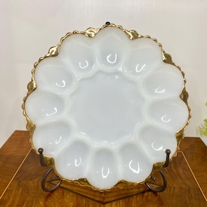 May include: White egg serving plate with a gold rim, displayed on a decorative metal stand. The plate has a scalloped edge and individual egg compartments. A classic piece for serving eggs or appetizers.