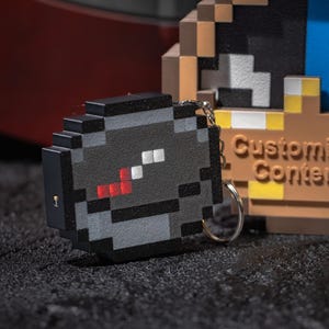May include: Pixelated compass keychain with a black, gray, and red design. Beside it is a pixelated clock with the text "Customized Content". The clock has brown, blue, and yellow accents. Both items are on a dark surface.
