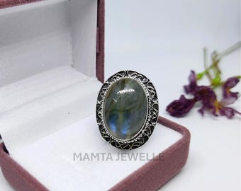 May include: A silver-toned ring with an oval, iridescent gemstone, set in an ornate, filigree-style frame. The ring is displayed in a velvet-lined jewelry box. The text "MAMTA JEWELLE" is visible.