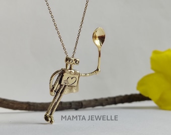 May include: Gold-toned robot pendant necklace. The robot has a heart-shaped detail and holds a spoon. The necklace is suspended from a delicate chain. The brand name "MAMTA JEWELLE" is printed at the bottom.
