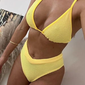 May include: A yellow bikini top and bottom with a textured fabric. The top is a triangle style with thin straps. The bottom is a high-waisted style with a V-shaped front.