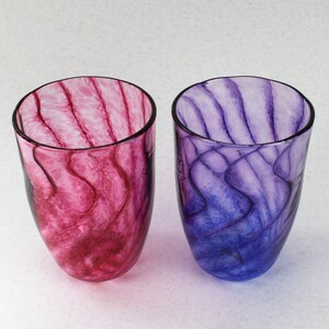 May include: Two glass tumblers with swirling patterns of pink and purple. The tumblers are clear glass with a translucent, marbled effect.