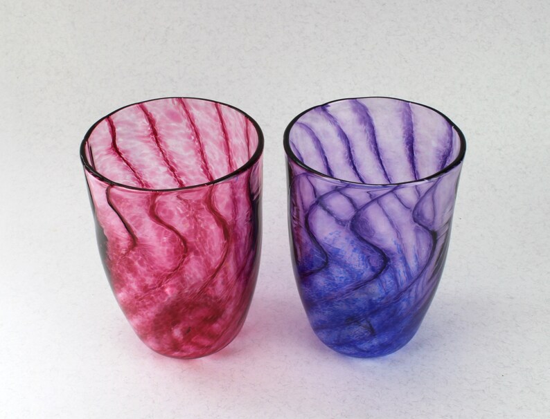 May include: Two glass tumblers with swirling patterns of pink and purple. The tumblers are clear glass with a translucent, marbled effect.