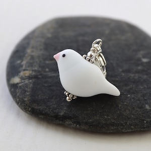 May include: A white ceramic bird charm with a pink beak and silver accents. The charm is attached to a silver lobster clasp.