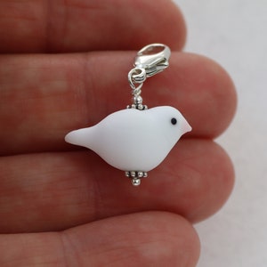 May include: White glass bird charm with a silver clasp. The bird has a black eye and a pink beak.