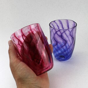 May include: Two glass tumblers with a swirling, marbled pattern. One tumbler is a deep red colour, and the other is a deep purple colour.