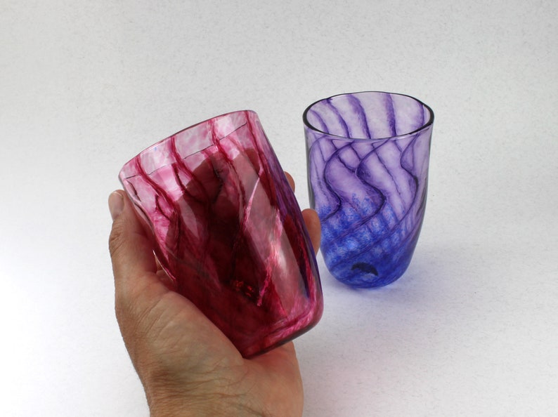 May include: Two glass tumblers with a swirling, marbled pattern. One tumbler is a deep red colour, and the other is a deep purple colour.