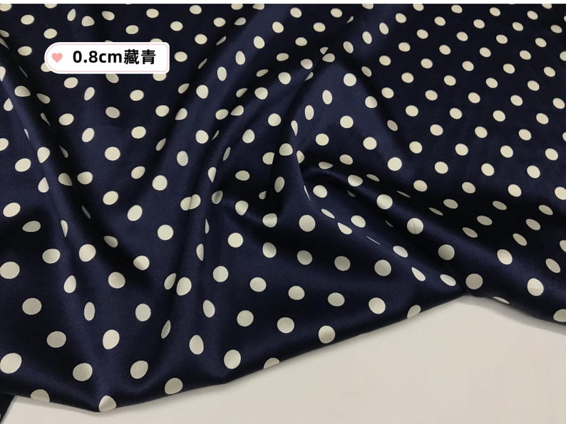 Peut inclure: Tissu bleu marine orn&eacute; de pois blancs. Le tissu pr&eacute;sente un aspect brillant, sugg&eacute;rant de la soie ou du satin. Le texte "0.8cm" est visible. Les pois mesurent environ 0,8 cm de diam&egrave;tre.