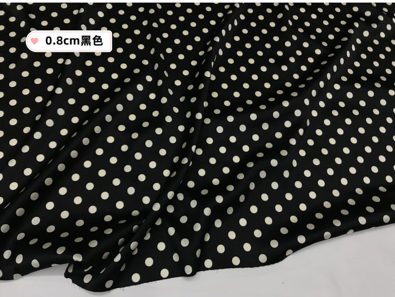 Peut inclure: Tissu noir &agrave; pois blancs. Les pois mesurent environ 0,8 cm de diam&egrave;tre. Le tissu est drap&eacute;, cr&eacute;ant des plis et des ombres. Le motif g&eacute;n&eacute;ral est un design &agrave; pois classique.