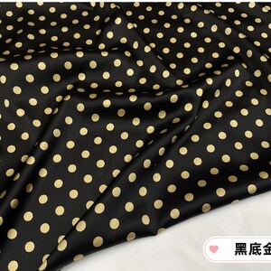 Peut inclure: Tissu noir orn&eacute; de pois dor&eacute;s espac&eacute;s r&eacute;guli&egrave;rement. Le tissu pr&eacute;sente une surface lisse et l&eacute;g&egrave;rement brillante, avec des plis et des froissements visibles. L'ensemble cr&eacute;e un motif classique et &eacute;l&eacute;gant.
