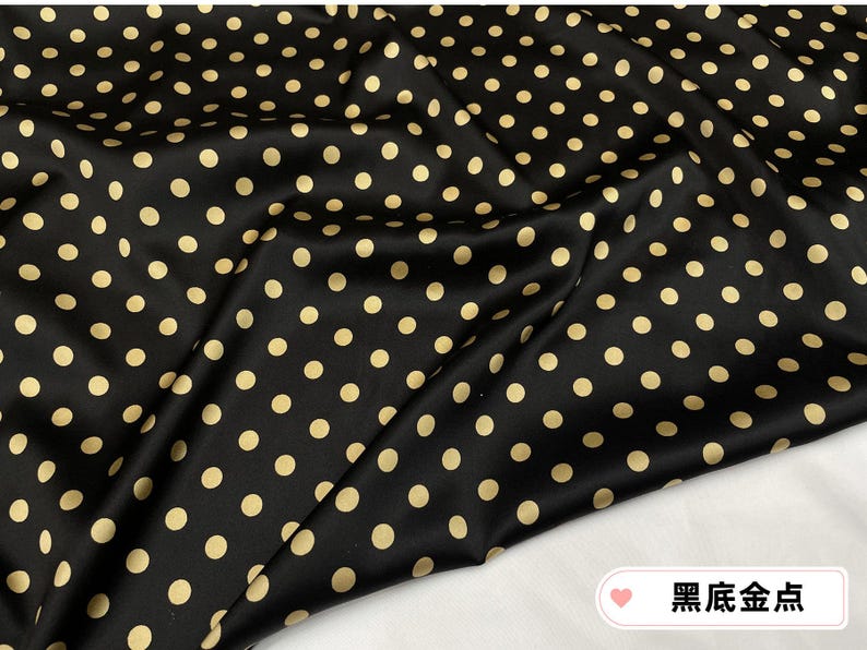 Peut inclure: Tissu noir orn&eacute; de pois dor&eacute;s espac&eacute;s r&eacute;guli&egrave;rement. Le tissu pr&eacute;sente une surface lisse et l&eacute;g&egrave;rement brillante, avec des plis et des froissements visibles. L'ensemble cr&eacute;e un motif classique et &eacute;l&eacute;gant.