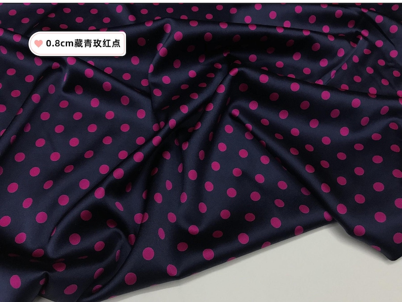 Peut inclure: Tissu bleu marine fonc&eacute; avec un motif de pois rose vif. Le tissu est pli&eacute;, montrant la texture et le lustre du mat&eacute;riau. Le texte sur l'image indique "0,8 cm de points bleu fonc&eacute; et rouges."