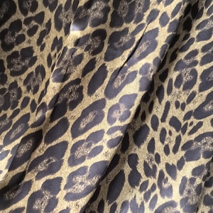 Może przedstawiać: Zbliżenie tkaniny z wzorem w cętki. Tkanina ma beżowe tło z ciemnobrązowymi plamami. Tkanina jest złożona, tworząc cienie i światła.