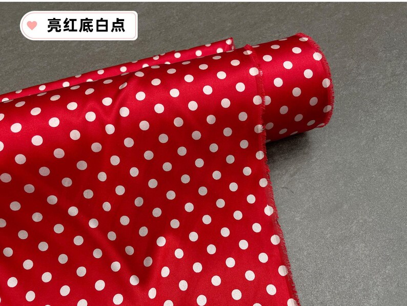 Peut inclure: Un rouleau de tissu rouge &agrave; pois blancs. Le tissu est pli&eacute;, r&eacute;v&eacute;lant le motif et le bord roul&eacute;. Le texte "亮红底白点" est visible dans le coin sup&eacute;rieur gauche.