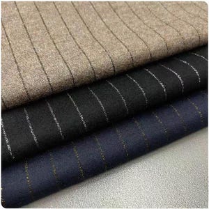 Könnte beinhalten: Nahaufnahme von drei Stoffmustern in Braun-, Schwarz- und Marineblautönen. Jeder Stoff weist vertikale Nadelstreifen in Metallic-Silber oder -Gold auf. Die Texturen scheinen Wolle oder ein ähnliches Material zu sein.
