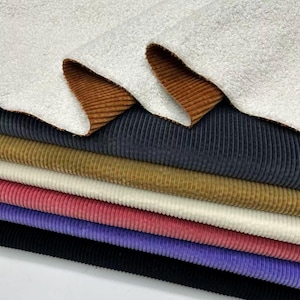 Puede incluir: Una pila de muestras de tela de pana coloridas. La capa superior es una tela blanca texturizada con un reverso de pana marrón. Debajo hay varios colores de pana, incluyendo azul marino, dorado, rosa y negro. Las telas están apiladas ordenadamente.