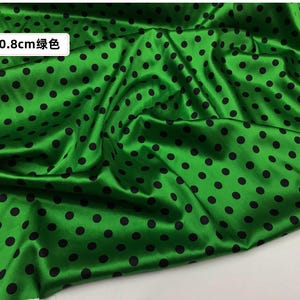 Peut inclure: Tissu satin&eacute; vert avec des pois noirs. Le tissu a une finition brillante et est drap&eacute;, cr&eacute;ant des plis souples. Les pois sont espac&eacute;s uniform&eacute;ment et mesurent 0,8 cm de diam&egrave;tre. Id&eacute;al pour la couture, l'artisanat ou la d&eacute;coration int&eacute;rieure.
