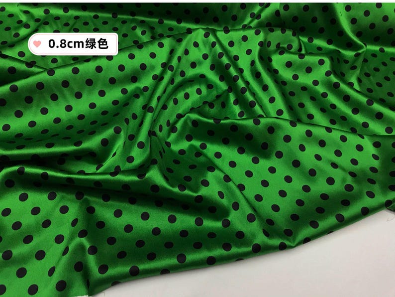 Peut inclure: Tissu satin&eacute; vert avec des pois noirs. Le tissu a une finition brillante et est drap&eacute;, cr&eacute;ant des plis souples. Les pois sont espac&eacute;s uniform&eacute;ment et mesurent 0,8 cm de diam&egrave;tre. Id&eacute;al pour la couture, l'artisanat ou la d&eacute;coration int&eacute;rieure.