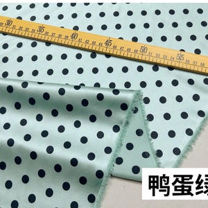 Peut inclure: Un tissu vert clair avec un motif r&eacute;p&eacute;t&eacute; de pois noirs. Une r&egrave;gle en bois avec des mesures en centim&egrave;tres est pos&eacute;e sur le tissu. Le tissu a une texture lisse, semblable &agrave; du satin. Le texte "鸭蛋绿" est dans un encadr&eacute; blanc en bas &agrave; droite.