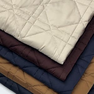 May include: A selection of quilted fabric in a range of colours. The top layer is a pale beige, with layers of burgundy, navy blue, and a warm brown beneath. Each piece has a diamond pattern created by stitched lines.