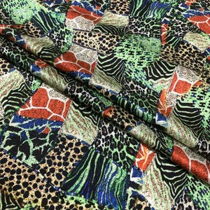 May include: A vibrant fabric with a patchwork design featuring animal print patterns. The design includes leopard spots, zebra stripes, and giraffe patterns in a mix of green, black, orange, and blue colors. The fabric is folded, showing its texture.
