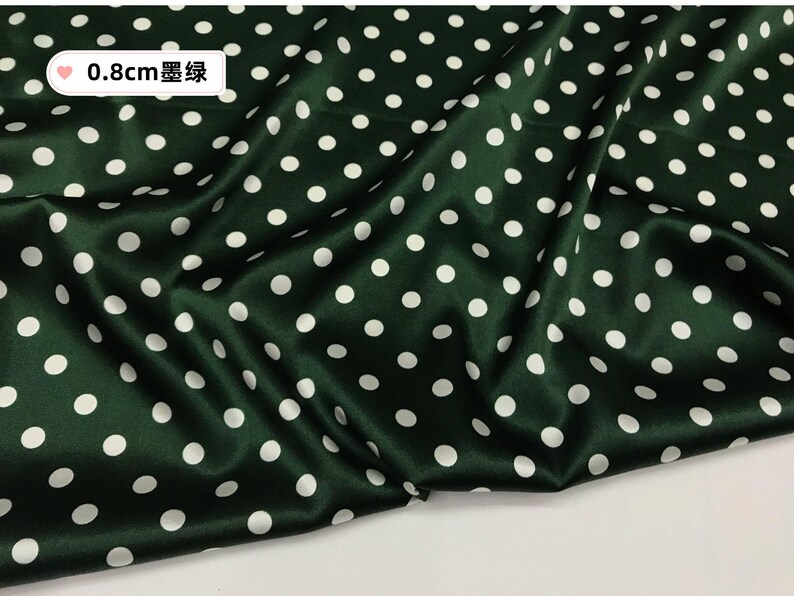 Peut inclure: Tissu vert fonc&eacute; &agrave; pois blancs. Le tissu a un aspect satin&eacute; et est drap&eacute;, montrant la texture et le flux du mat&eacute;riau. Le texte sur l'image indique "0,8 cm 墨绿".
