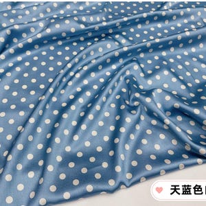 Peut inclure: Gros plan sur un tissu bleu avec des pois blancs. Le tissu est drap&eacute;, cr&eacute;ant des plis et des ombres douces. Le tissu a un aspect brillant, semblable &agrave; du satin. Le texte sur l'image dit "Polka Dots Bleu Ciel".