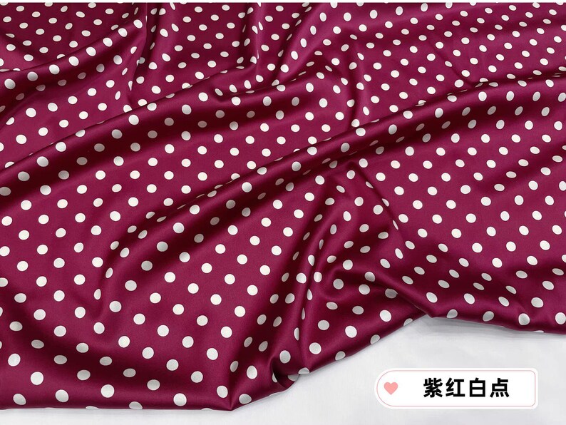 Peut inclure: Tissu bordeaux &agrave; pois blancs. Le tissu est drap&eacute;, cr&eacute;ant des plis et des ombres. Les pois sont espac&eacute;s uniform&eacute;ment et de taille constante, ajoutant un &eacute;l&eacute;ment ludique au design. Le tissu a un l&eacute;ger &eacute;clat.