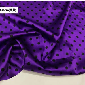 Peut inclure: Un tissu violet vif avec un aspect brillant, orn&eacute; de pois noirs espac&eacute;s r&eacute;guli&egrave;rement. Le tissu est pli&eacute;, cr&eacute;ant des ombres et des reflets. Le texte sur l'image indique "0,8 cm".